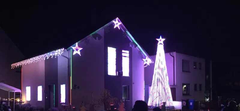 Haus in violettem Licht mit Pixel-Sternen und einem Lichterbaum