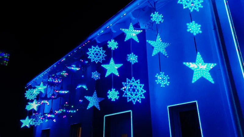 Blau leuchtende Schneeflocken und Sterne aus Pixeln an einer Hauswand